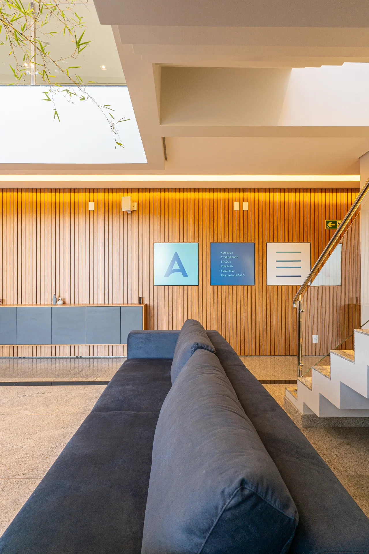 Hall de entrada do projeto AES com painel ripado em madeira, sofá escuro e claraboia